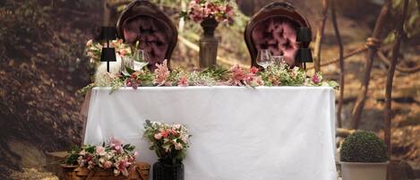 Una mesa cubierta con un mantel blanco, rodeada de sillas y decorada con flores y una pequeña planta en maceta.