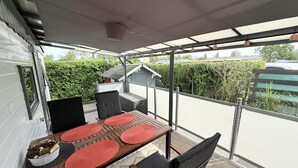 A covered outdoor dining area with a table and chairs, a potted plant, and a view of a residential neighborhood. - Beach Resort Kamperland - 771 (Kamperland)