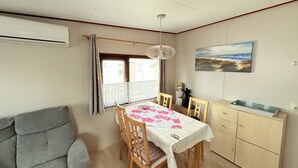 A dining area with a table set for four, wooden chairs, a grey sofa, a wooden cabinet, and a painting of a beach scene. - Beach Resort Kamperland - 771 (Kamperland)