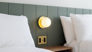 A neatly made bed with white linens, a bedside table with a lamp, and a wall-mounted light fixture.