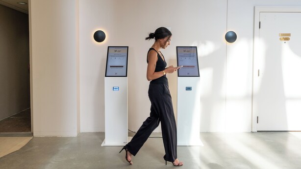 A woman walking past self-check-in kiosks in a hotel lobby.