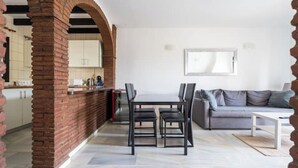 Een moderne leefruimte met een eethoek, een bank en een keuken, zichtbaar door een boog.