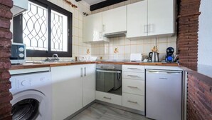 Een kleine keuken met witte kasten, een inbouwoven, een vaatwasser en een wasmachine.