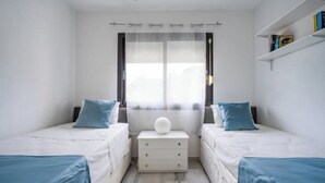 Een slaapkamer met twee bedden, een nachtkastje, een raam met gordijnen en een boekenkast.