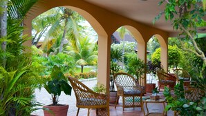 Un espace extérieur aménagé, abrité et doté de chaises et de tables, entouré d’une végétation luxuriante et de plantes en pot.