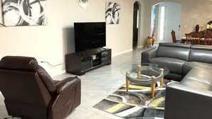 A modern living room with a leather sofa, a glass coffee table, and abstract wall art. - Delightful 2 bdrm home in peaceful area w/parking (ZEPHYRHILLS)