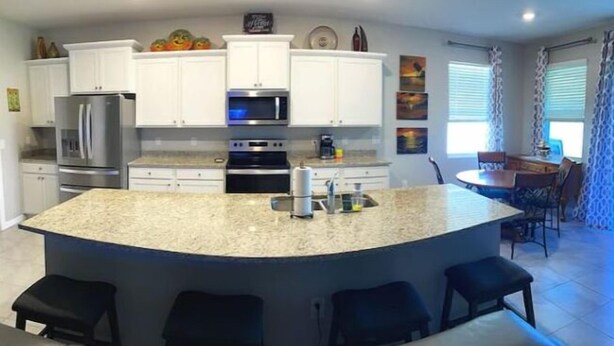 A modern kitchen with white cabinets, stainless steel appliances, and a central island with bar stools. - Delightful 2 bdrm home in peaceful area w/parking (ZEPHYRHILLS)