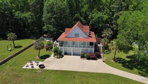 A two-story house with a red roof, surrounded by lush greenery and a well-maintained lawn.