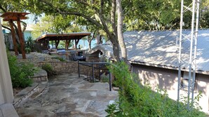Um alpendre de pedra com pérgola, uma área de estar coberta e vista para a água.
