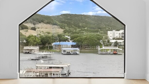 Vista através de uma janela triangular de um lago com barcos e edifícios ao fundo.