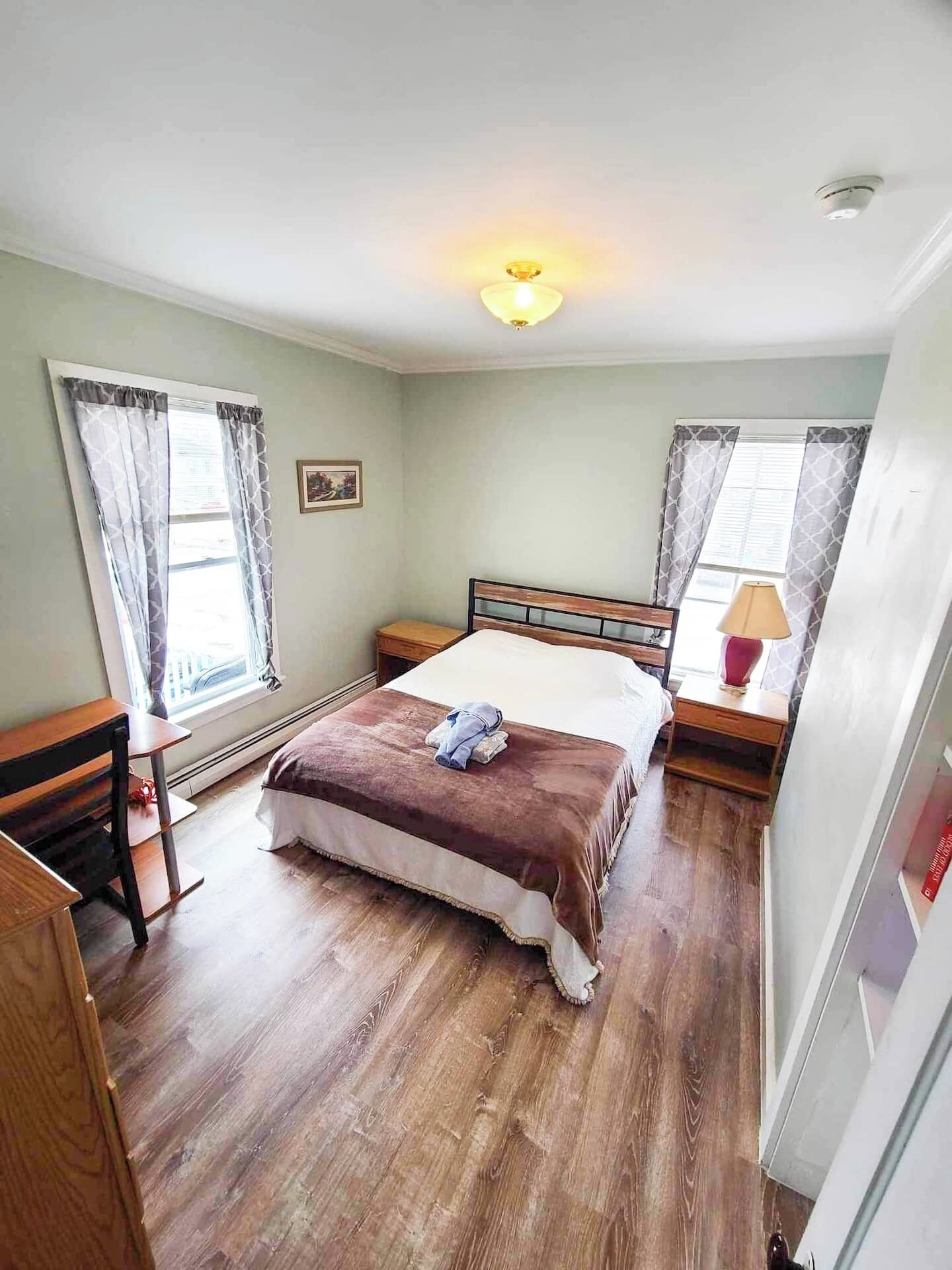 A bedroom with a bed, bedside tables, a desk, and a window with curtains.