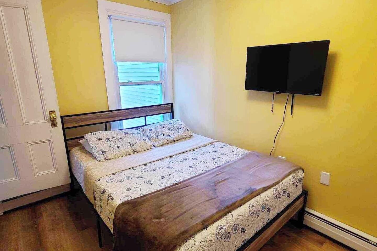 Une chambre à coucher avec un lit, une fenêtre, une porte et un téléviseur fixé au mur.