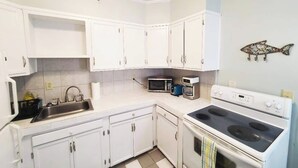 Una cocina con armarios blancos, un lavamanos, un microondas, un tostador y una estufa.