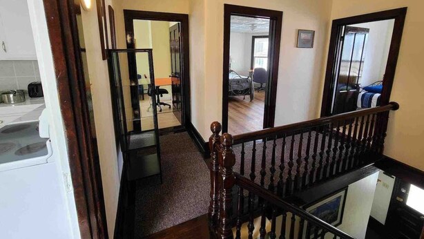 Una escalera conduce a un segundo piso con barandilla de madera, una zona de cocina con un tostador y una pared espejada que refleja una habitación con una cama y una silla.