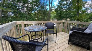 Eine Holzterrasse mit Korbmöbeln, darunter ein runder Tisch und zwei Stühle.