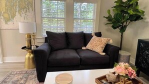 Ein Wohnzimmer mit einem dunkelgrauen Sofa, einem weißen Couchtisch, einer großen Pflanze und einer Karte an der Wand.