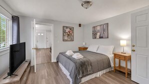 Une chambre à coucher comprenant un lit, un téléviseur, une table de chevet et une porte donnant sur une autre pièce.