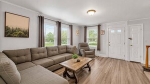 Un salon comprenant un canapé d’angle, une table basse en bois, un fauteuil inclinable et une porte dotée d’une poignée décorative.