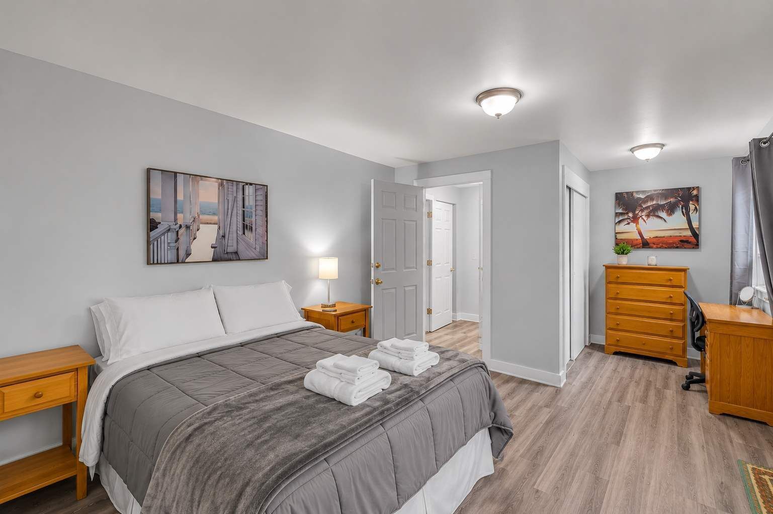 A bedroom with a bed, bedside tables, a dresser, a desk, and a painting on the wall.