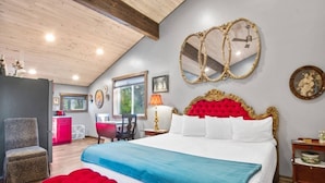 A bedroom with a large bed, a red upholstered bench, a wooden ceiling, and a view of the kitchen in the background. - Roses Old West Cabin Private Hot Tub Glacier NP (Columbia Falls)