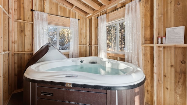 A wooden cabin with a hot tub, wooden walls, and windows with curtains. - Roses Old West Cabin Private Hot Tub Glacier NP (Columbia Falls)