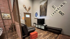 A room with a brick wall, a television, a bench, and a red crate.
