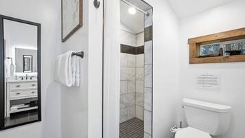 Un baño moderno con ducha envuelta en vidrio, inodoro blanco y estante de madera sobre el lavamanos.