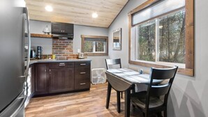 A kitchen with wooden cabinets, a refrigerator, a dining table with chairs, and a window with a view of trees.