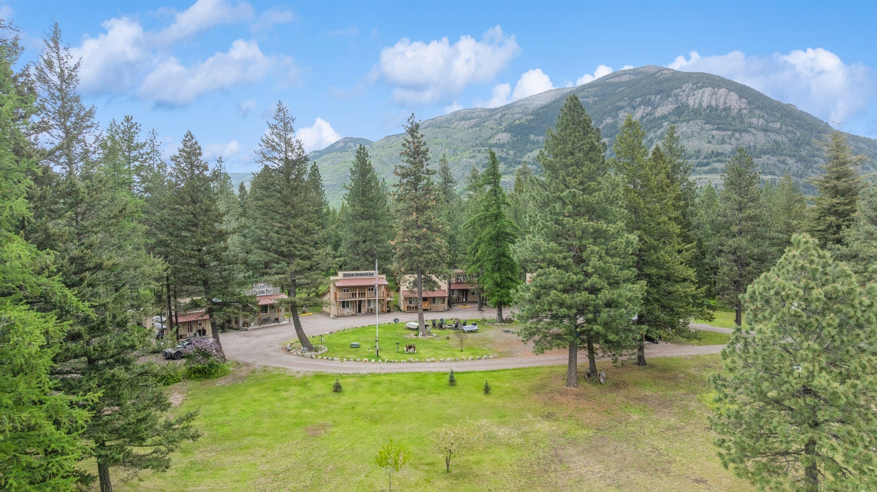 Un chalet doté d’un bâtiment principal entouré d’arbres, d’une zone herbeuse et d’une montagne en arrière-plan.