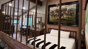 A room with a bed, a painting, a dining area, and a view of the outside.