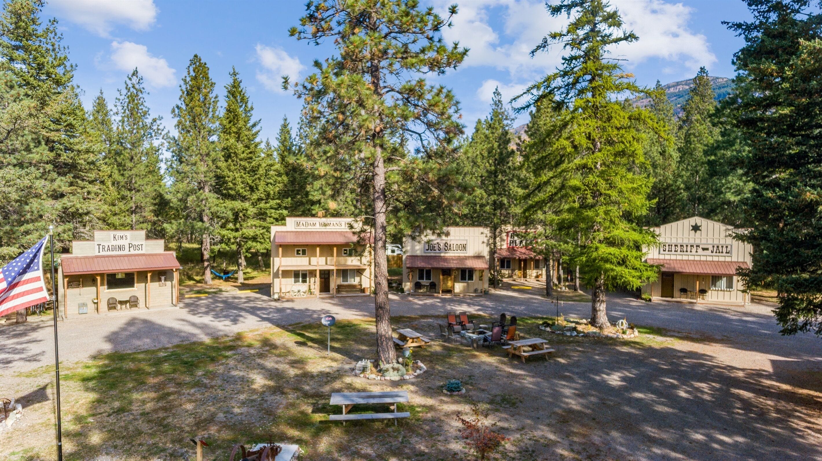 A rustic trading post with a flagpole, picnic tables, and a small building labeled "Sheriff Jail".