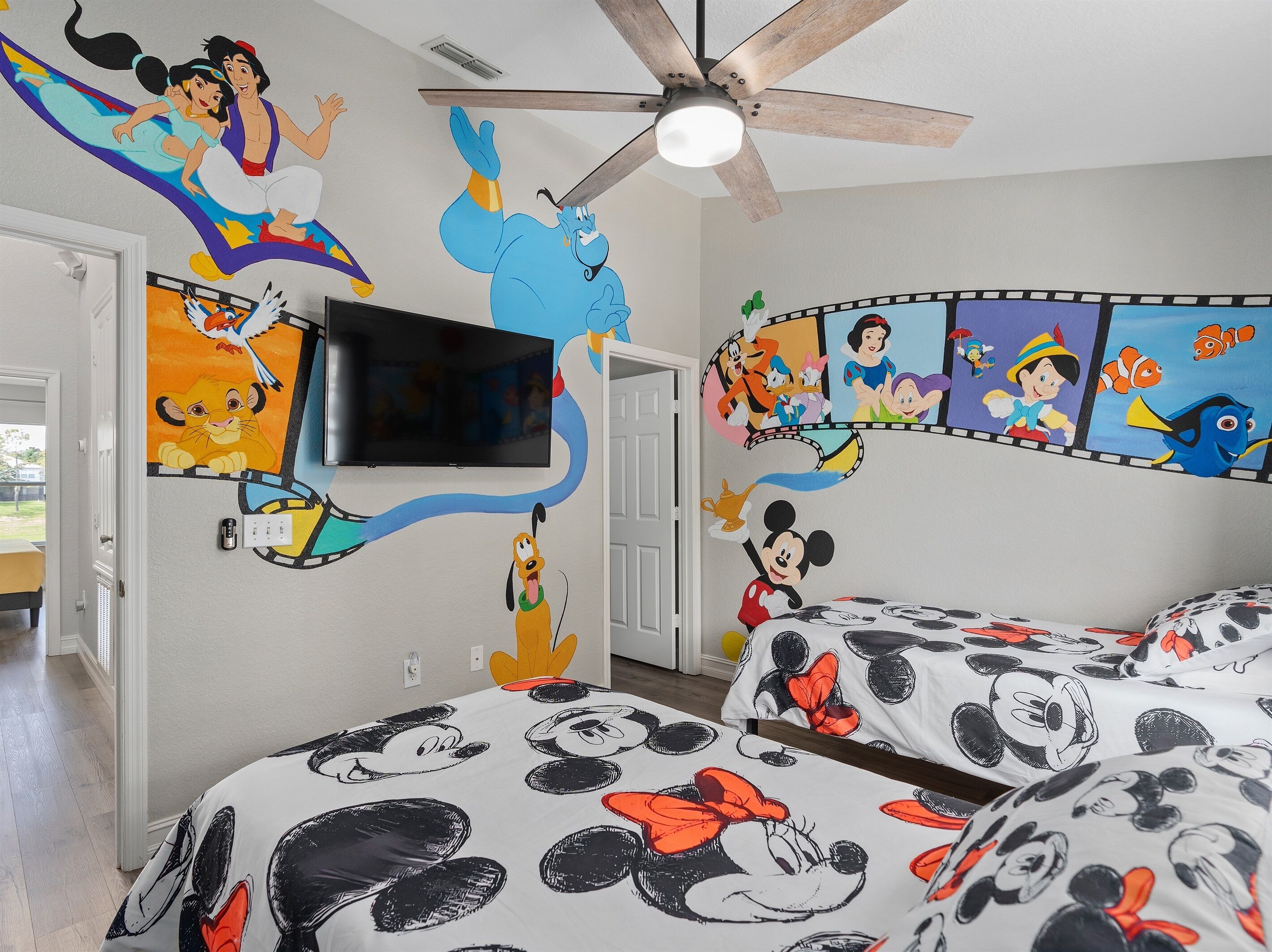 Une chambre à coucher décorée avec des motifs Disney sur les murs, dotée d’un ventilateur de plafond et de linge de lit à l’effigie de Mickey Mouse.