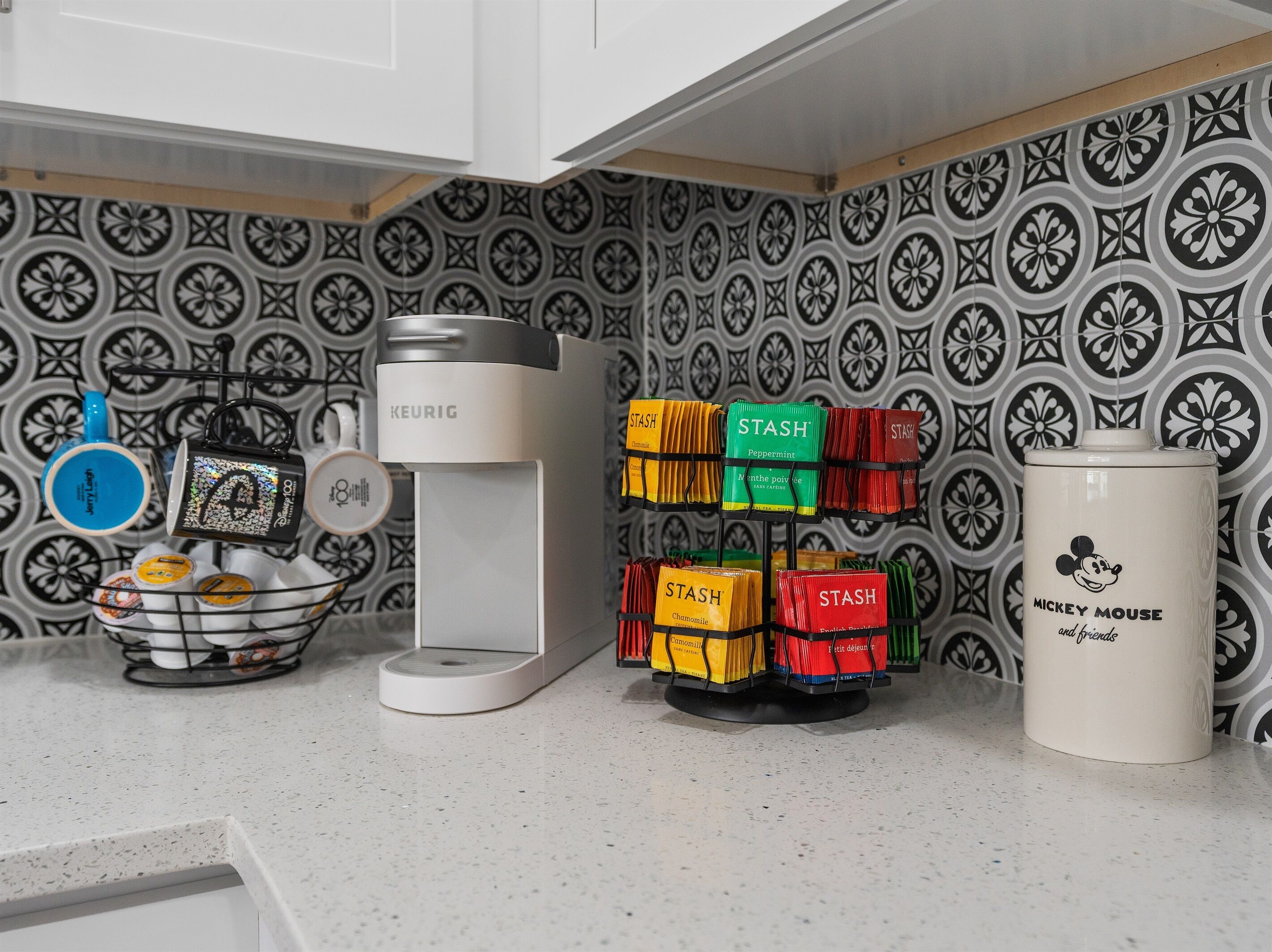 A kitchen with a Keurig coffee maker, a Mickey Mouse mug, and a coffee bean dispenser with various flavors.
