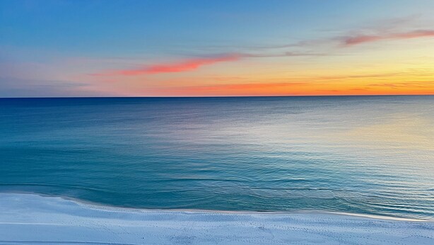 En strand med krystalklart hav og en solnedgang i baggrunden.