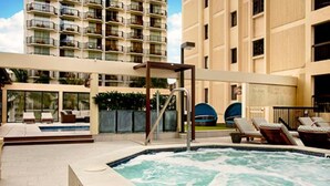 A hotel pool area with a hot tub, lounge chairs, and a view of a high-rise building in the background.
