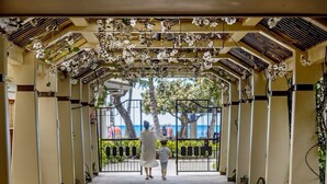 A covered walkway with a view of the sea, flanked by columns and plants.