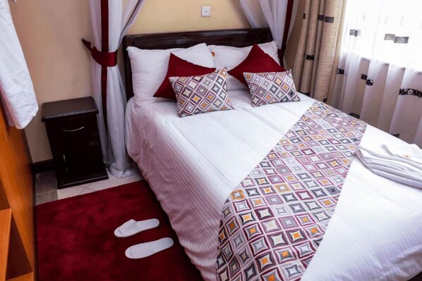 A neatly made bed with patterned bedding, a bedside table, and a red rug.