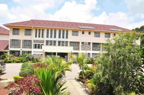 A multi-story building with a flat roof, solar panels, and a well-maintained garden with various plants and a paved driveway. - The Radix Hotel  (Nairobi)