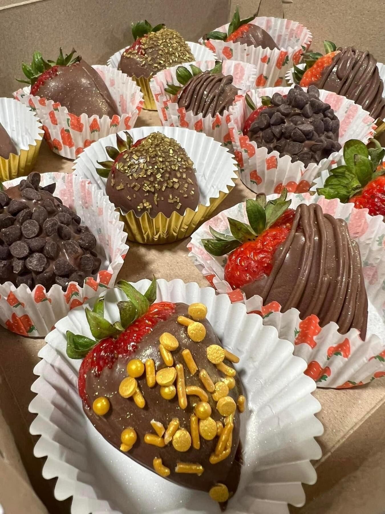 A box of assorted chocolate-covered strawberries and chocolates in paper cups.