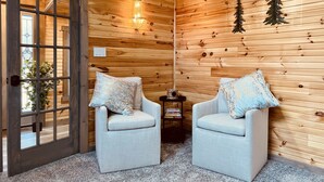 Een knus vertrek met houten wanden, twee fauteuils met opvallende kussens, een tafeltje met boeken en een decoratieve kerstboom.