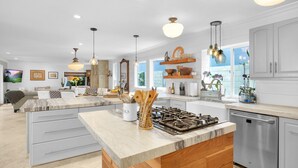Een moderne keuken met een centraal eiland, roestvrijstalen apparatuur en hangende lampen.