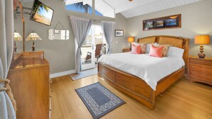 Een slaapkamer met een groot bed, houten hoofdbord, plafondventilator en uitzicht op de omgeving.