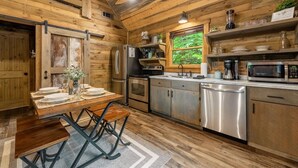 A rustic wooden cabin kitchen with a dining table set for four, a refrigerator, stove, microwave, and dishwasher.