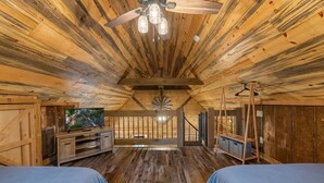 A cabin with a wooden interior, a ceiling fan, a television, and a staircase leading to a loft area.