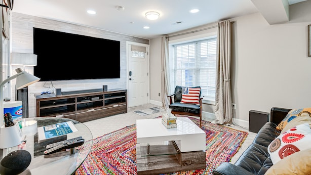 A modern living room with a large flat-screen TV, a sofa, a coffee table, and a colorful rug.