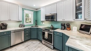 A kitchen with teal cabinets, a stainless steel range, a microwave, and a coffee maker.