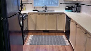 A kitchen with wooden cabinets, a black refrigerator, a sink, and a window with blinds. - Family Friendly, Gated Yard for Pets, Outdoor Firepit! (Calgary)
