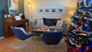 A living room with a piano, a Christmas tree, and a sofa with cushions. - Family Friendly, Gated Yard for Pets, Outdoor Firepit! (Calgary)