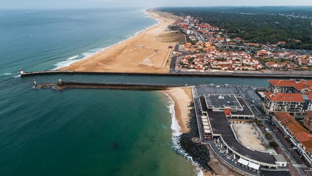Vista aérea de un pueblo costero con playa, muelle y edificios residenciales.
