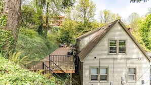 Une maison dotée d’une terrasse en bois, entourée d’une végétation luxuriante et d’arbres.